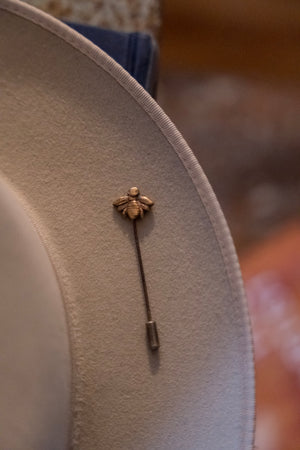 Close-up of a beige hat with a decorative bee pin on a blurred background