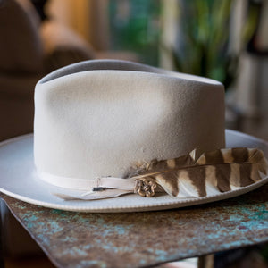 White fedora hat with a feather on a rustic wooden table