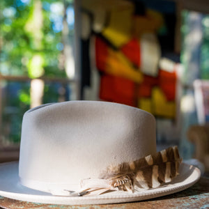 White hat with feather detail on a table in a room with colorful abstract art in the background