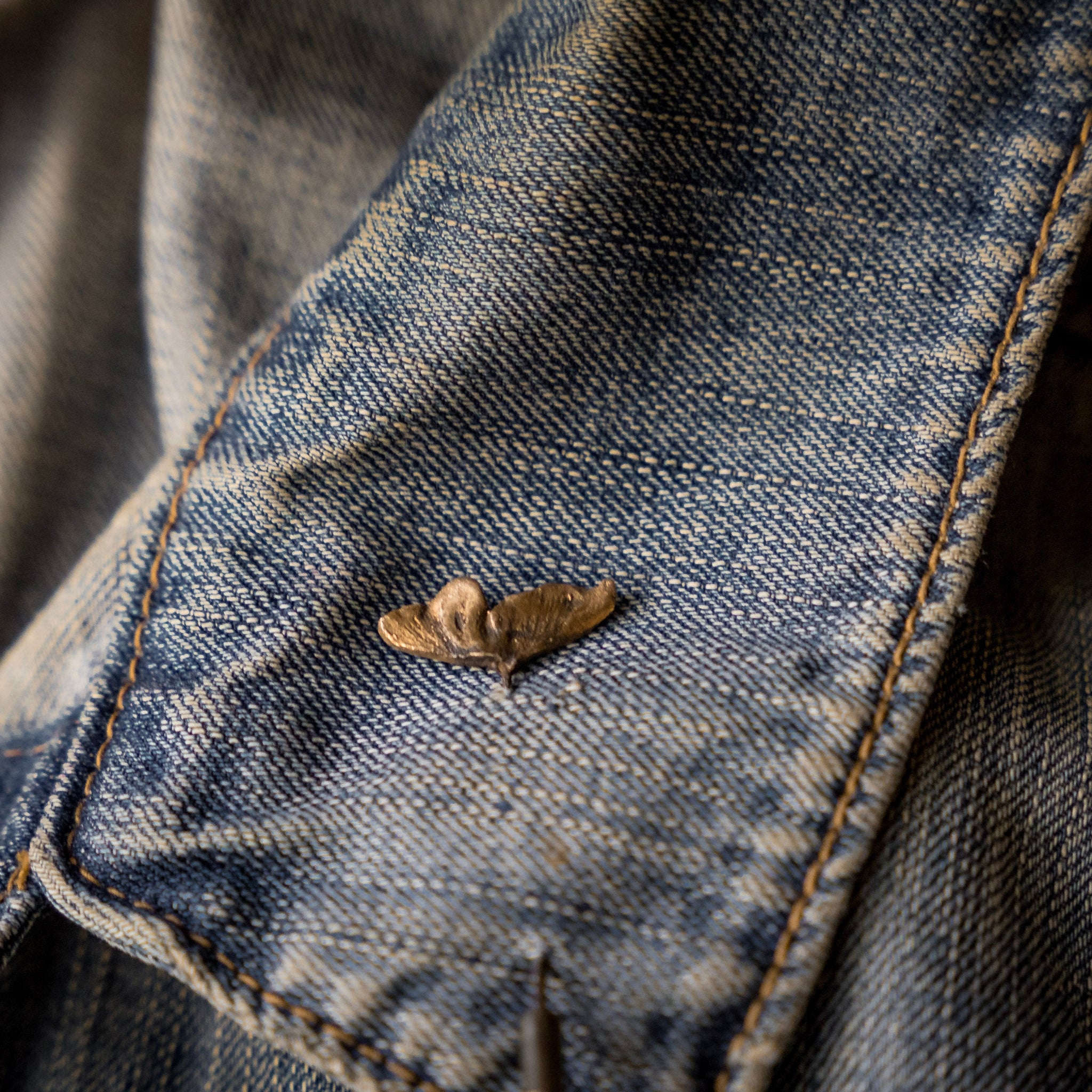 Close-up of a worn denim jacket with a button and stitching detail.