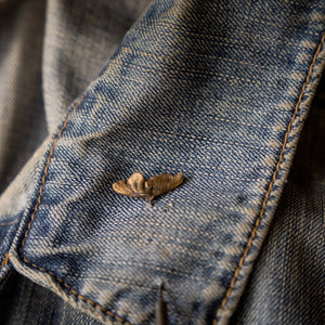 Close-up of a worn denim jacket with a button and stitching detail.